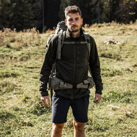 Man wearing dark outdoor shorts with hiking backpack in natural field setting