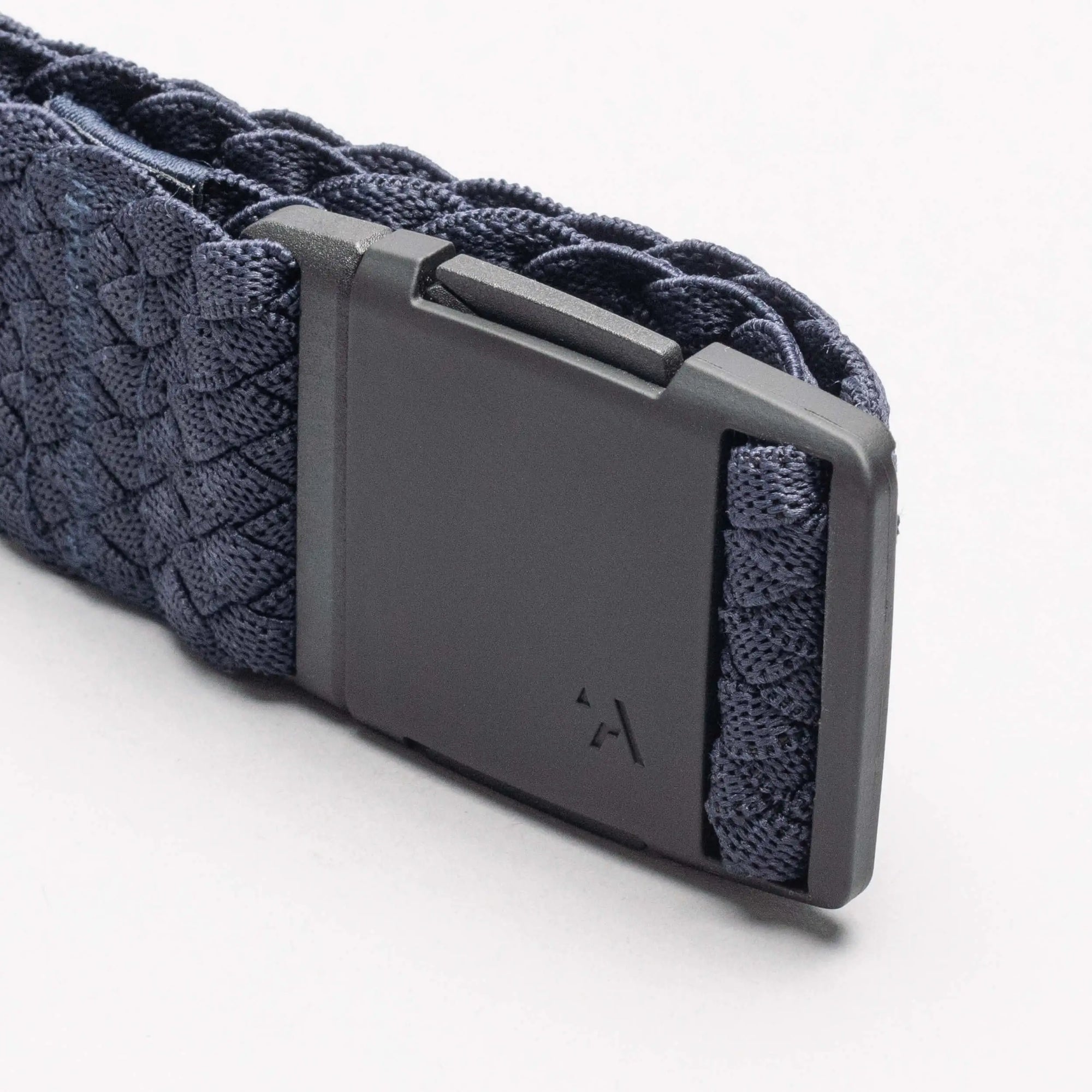 Close-up of woven fabric belt with dark rectangular buckle showing minimal logo detail