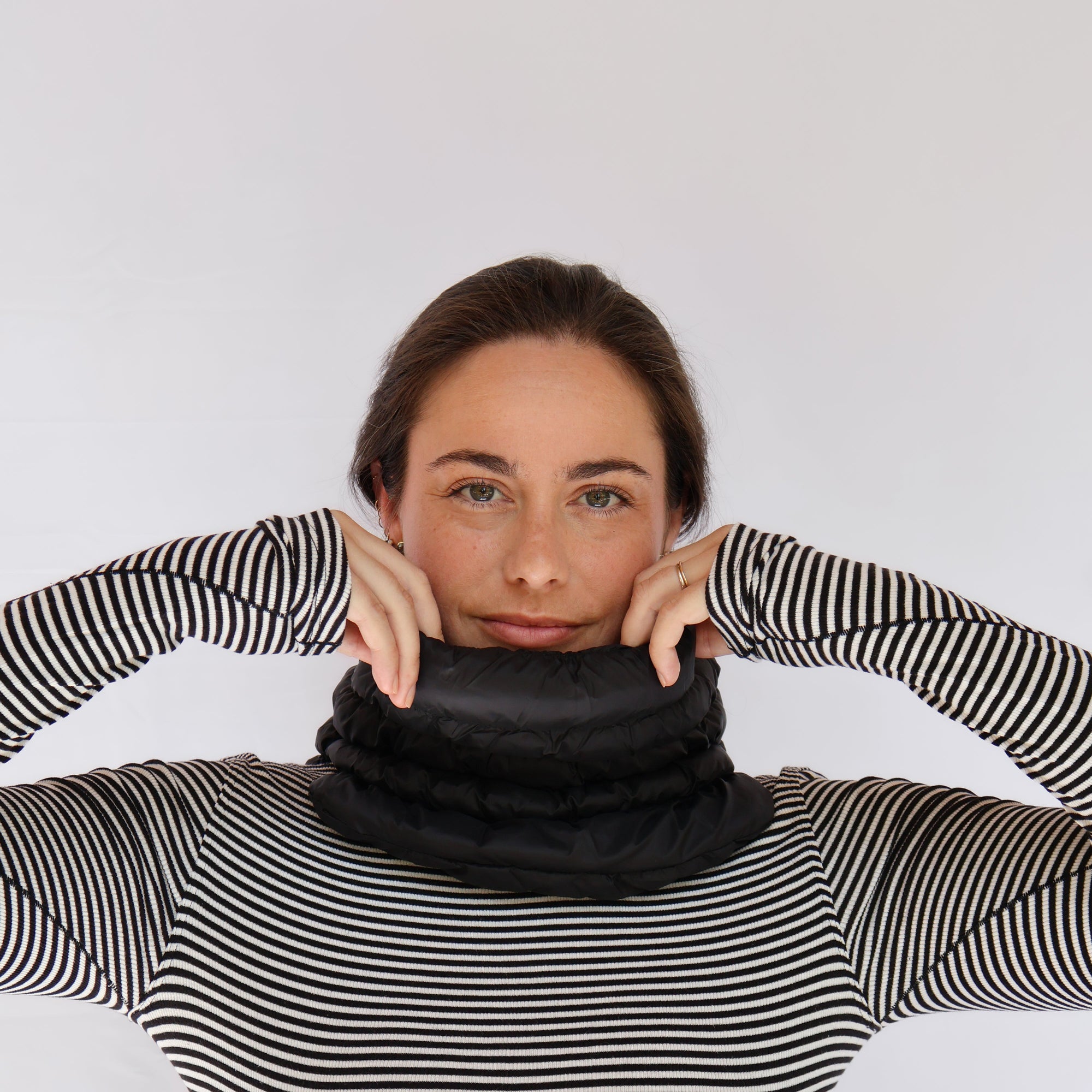 Black puffer neck gaiter worn by model, pulled up to chin, front view