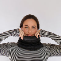 Black puffer neck gaiter worn by model, pulled up to chin, front view