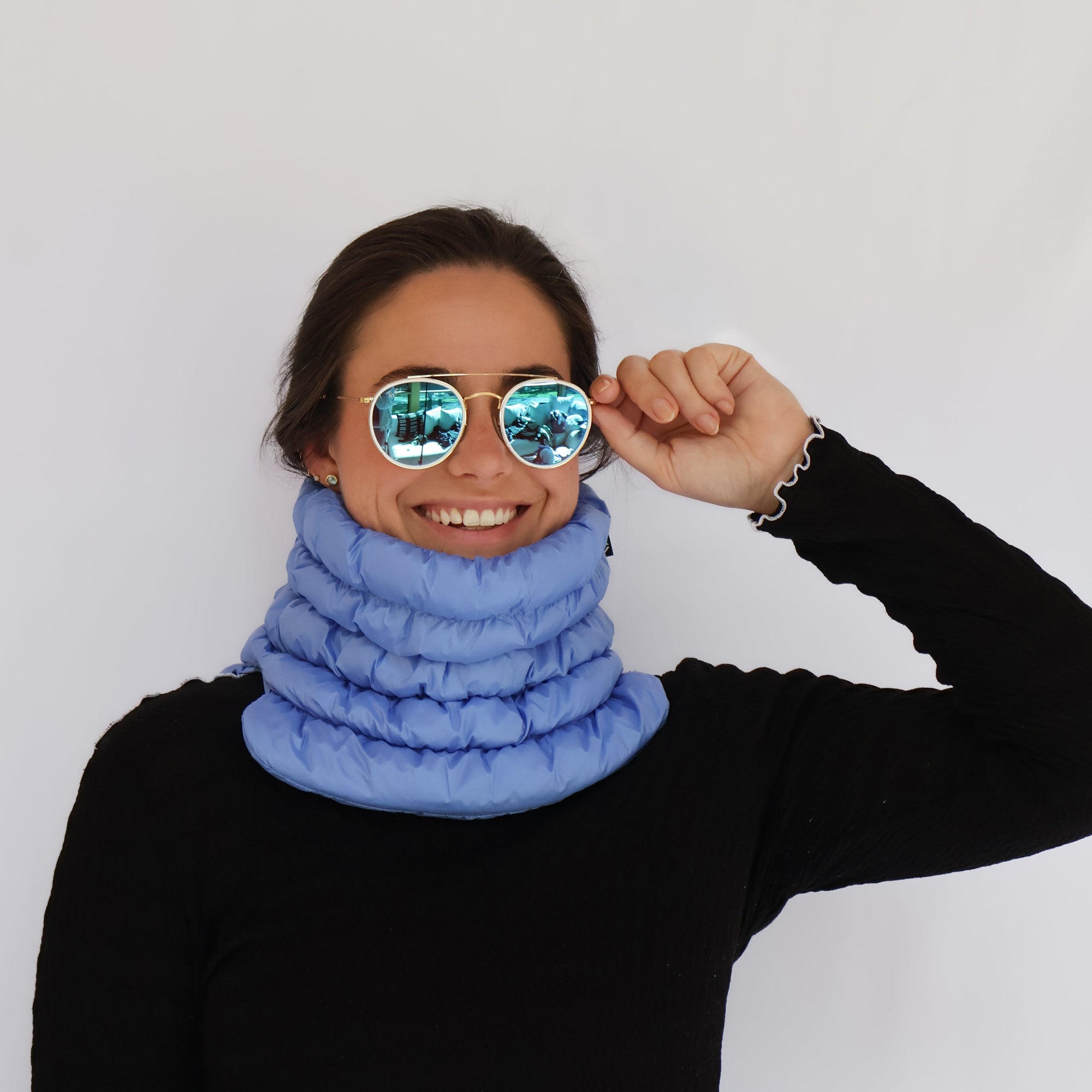 Light blue puffer neck gaiter worn by smiling model with mirrored aviator sunglasses