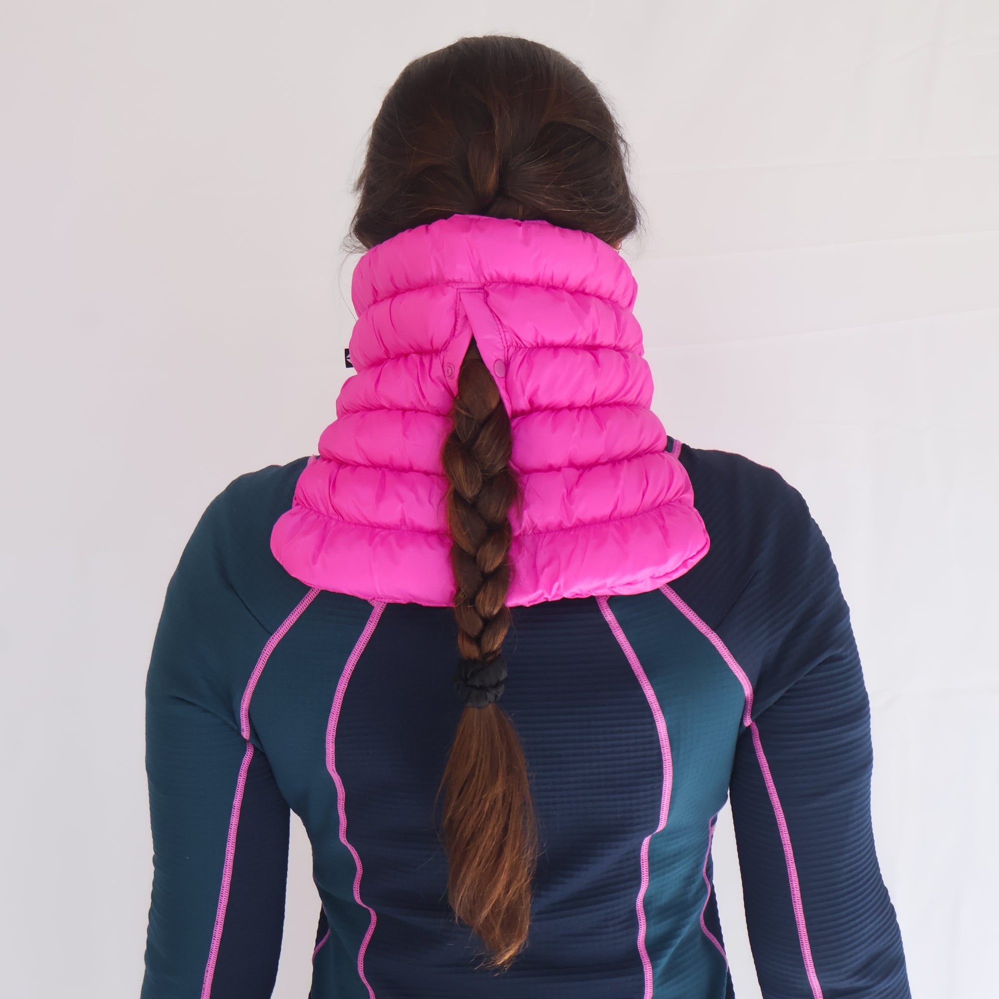 Quilted puffer neck gaiter in bright pink, shown from behind on model with braided hair