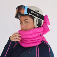 Bright pink quilted puffer neck gaiter worn on model with ski helmet, three-quarter view