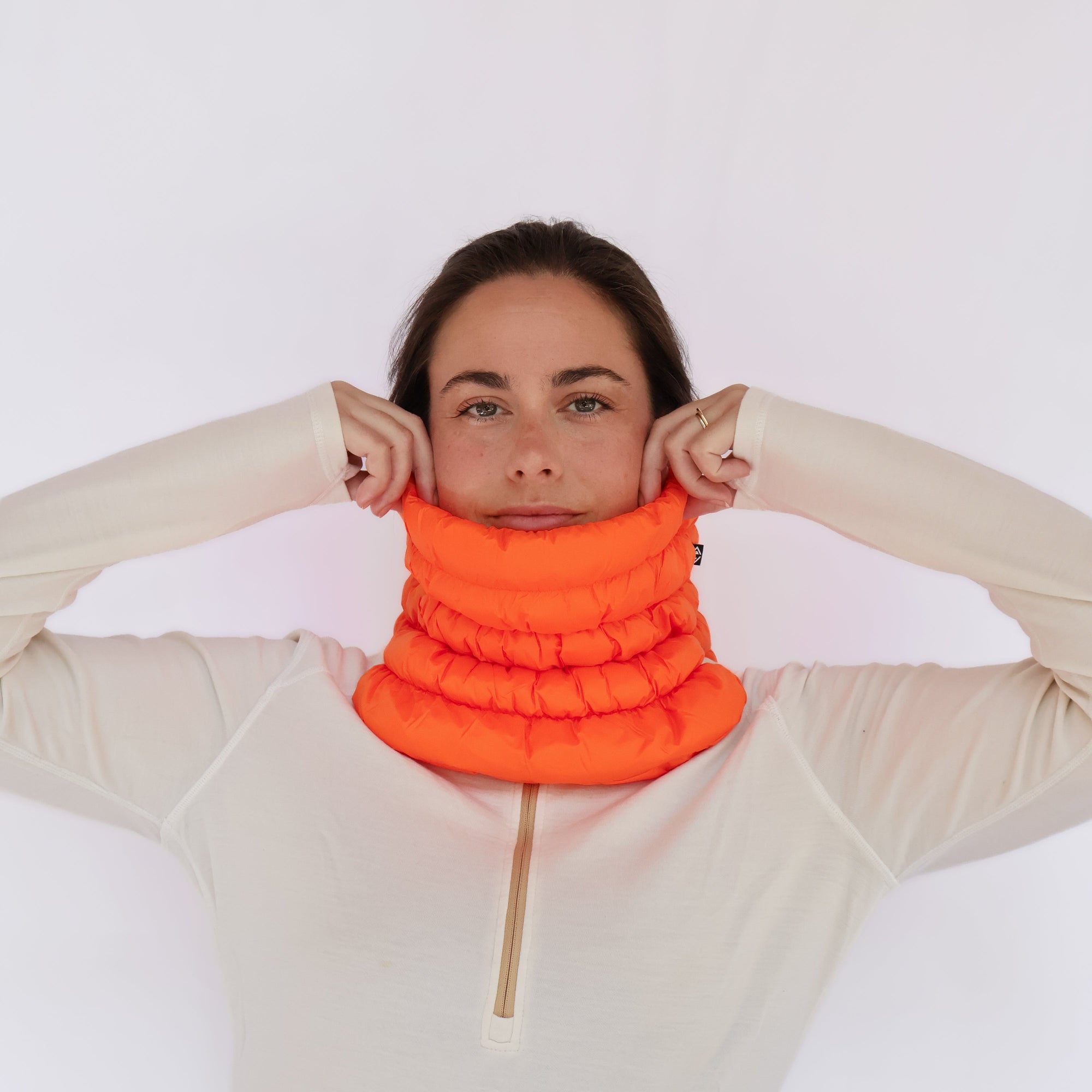 Bright orange puffer neck gaiter worn by model, adjusting fit with both hands
