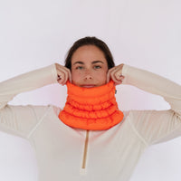 Bright orange puffer neck gaiter worn by model, adjusting fit with both hands