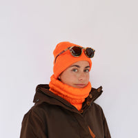 Bright orange puffer neck gaiter worn as a neckwarmer on a model with matching orange beanie