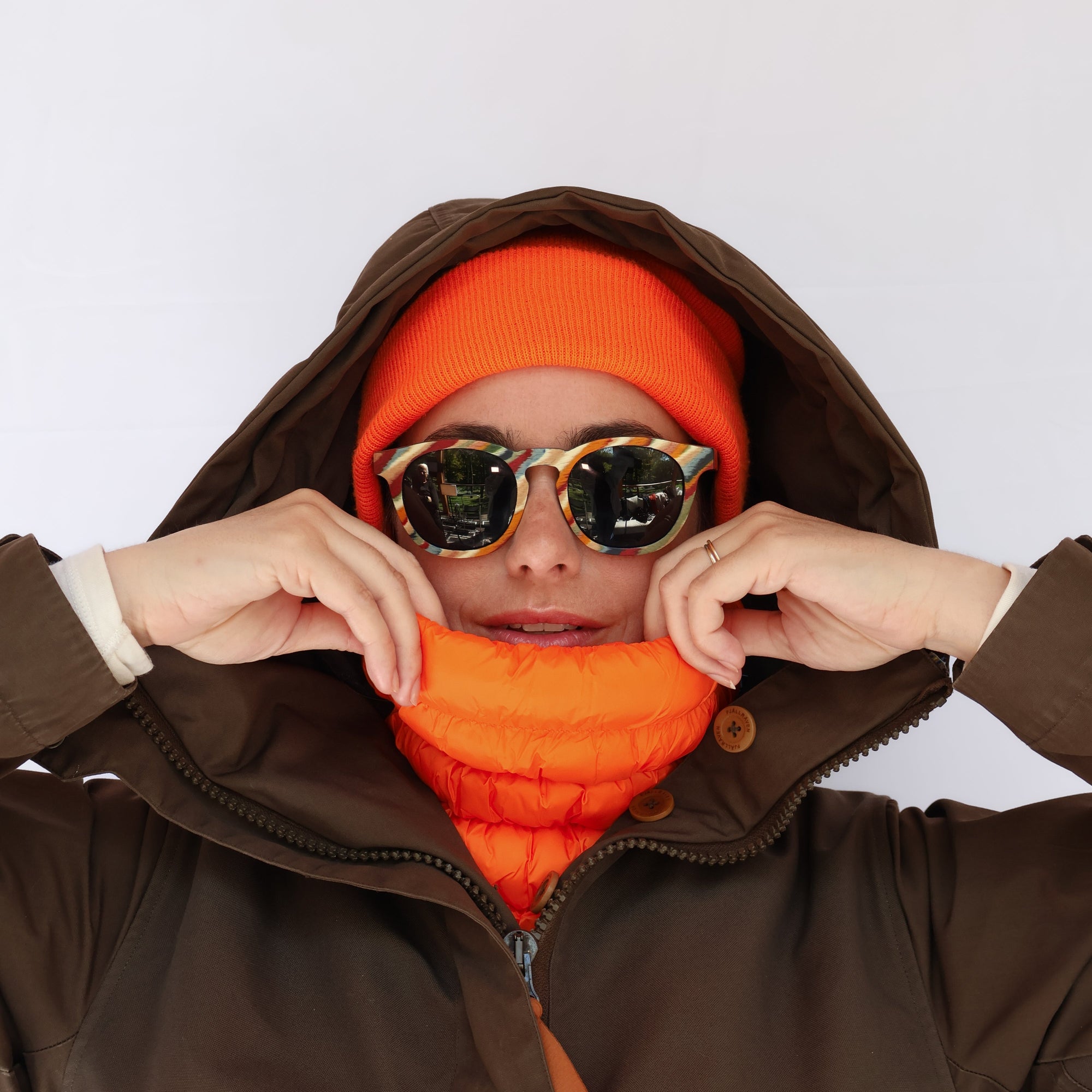 Bright orange puffer neck gaiter worn by model with matching orange beanie and sunglasses