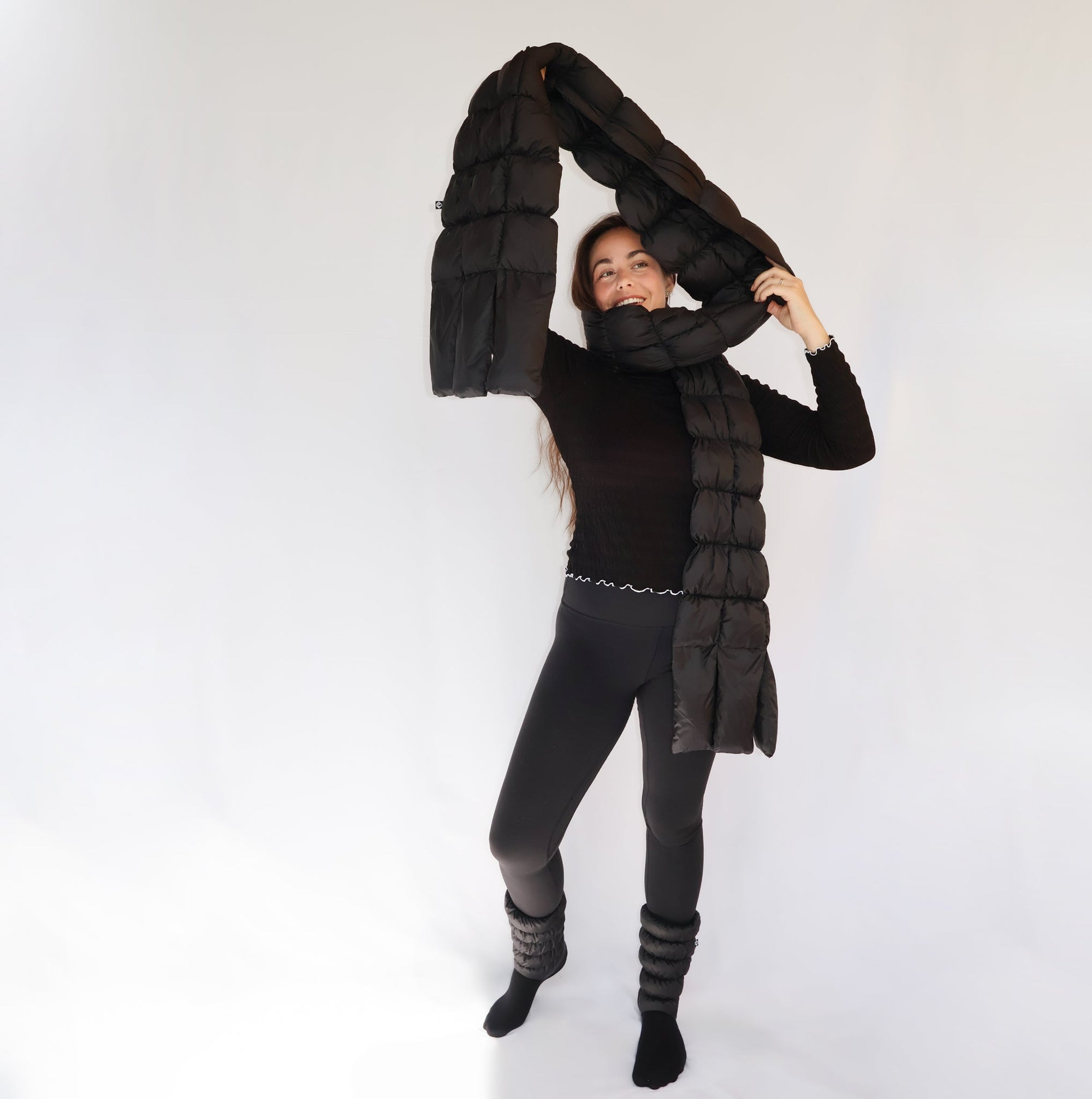 Model holding up long quilted puffer scarf overhead, worn around neck, full length view