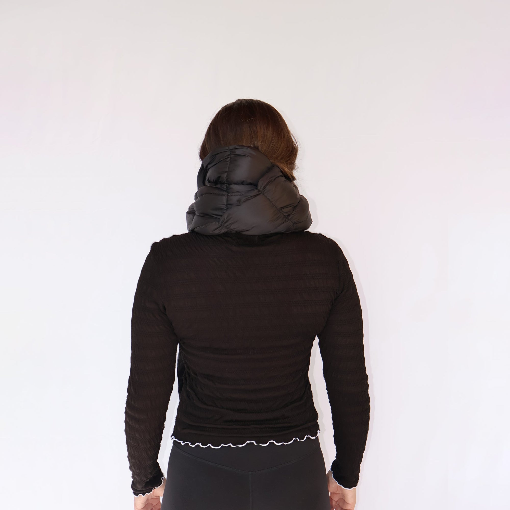 Black puffy quilted neck scarf worn on model, back view, with long-sleeve top