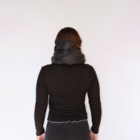 Black puffy quilted neck scarf worn on model, back view, with long-sleeve top