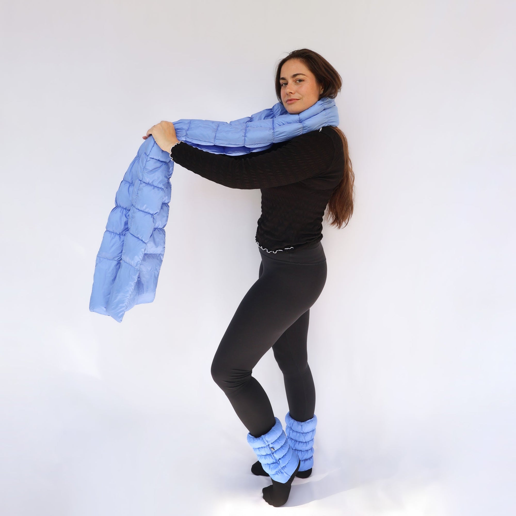 Model wearing a light blue quilted puffy scarf draped around neck, with matching puffy leg warmers