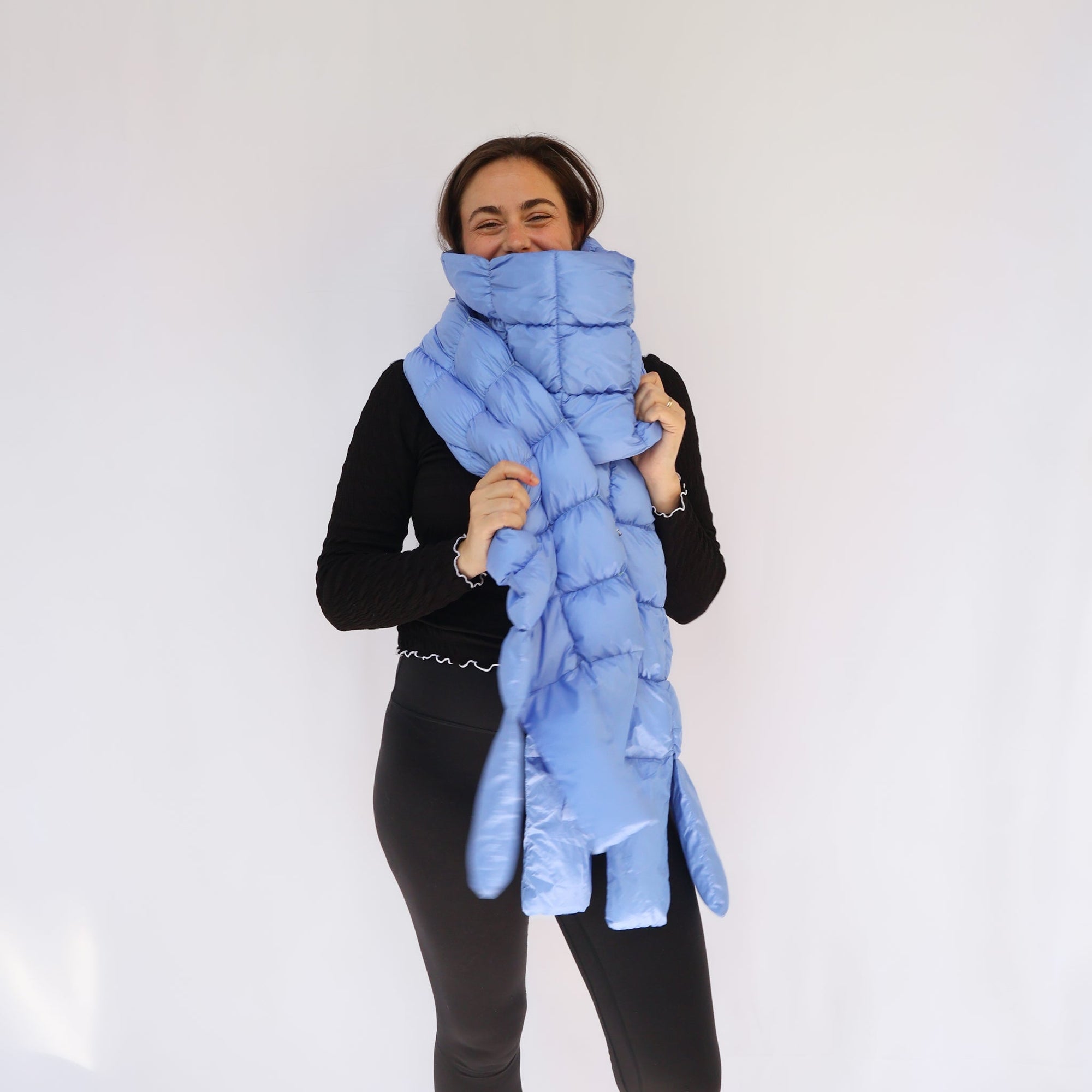 Woman smiling while wearing an oversized light blue quilted puffer scarf wrapped around her neck