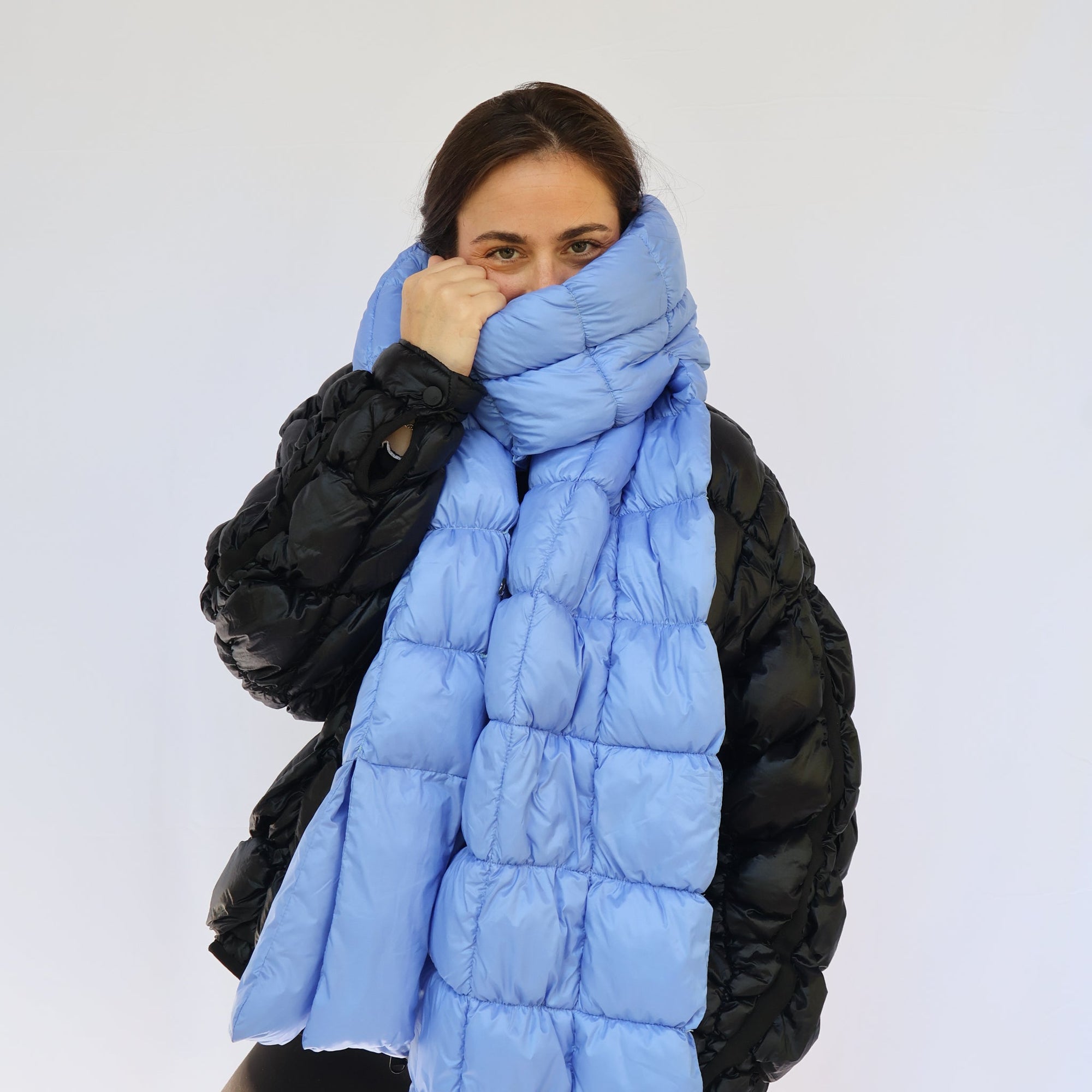 Model wearing a light blue quilted puffer scarf pulled up over her face, front view