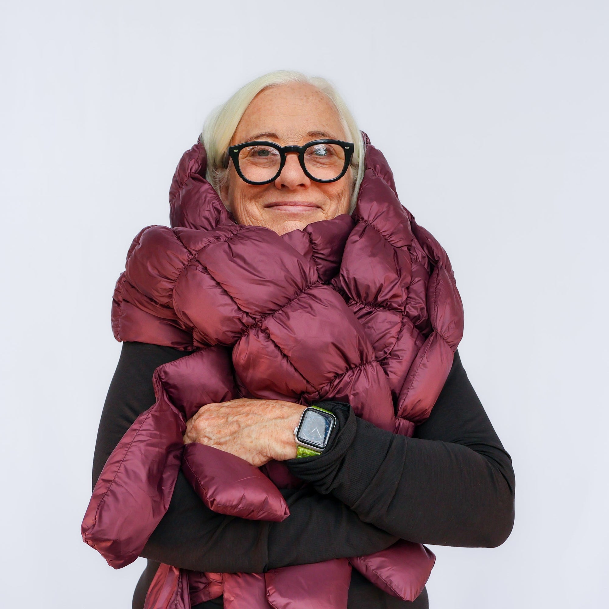 Woman wearing oversized puffy quilted scarf in deep burgundy, wrapped around shoulders and arms