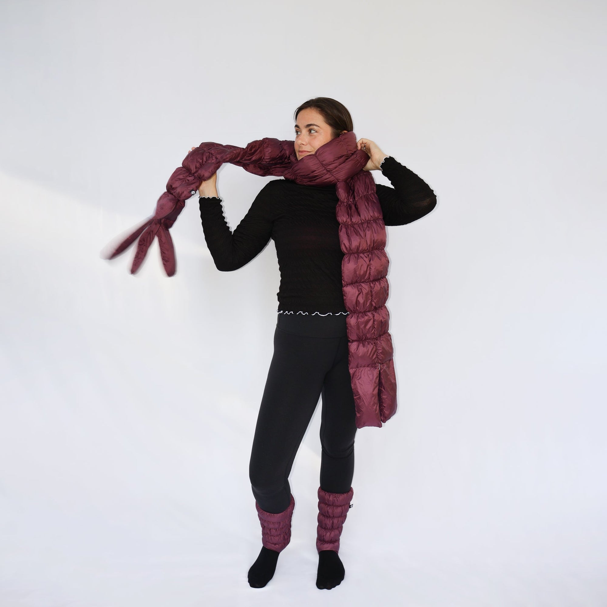 Model wearing an extra-long quilted puffer scarf in deep plum, styled around neck and trailing to floor