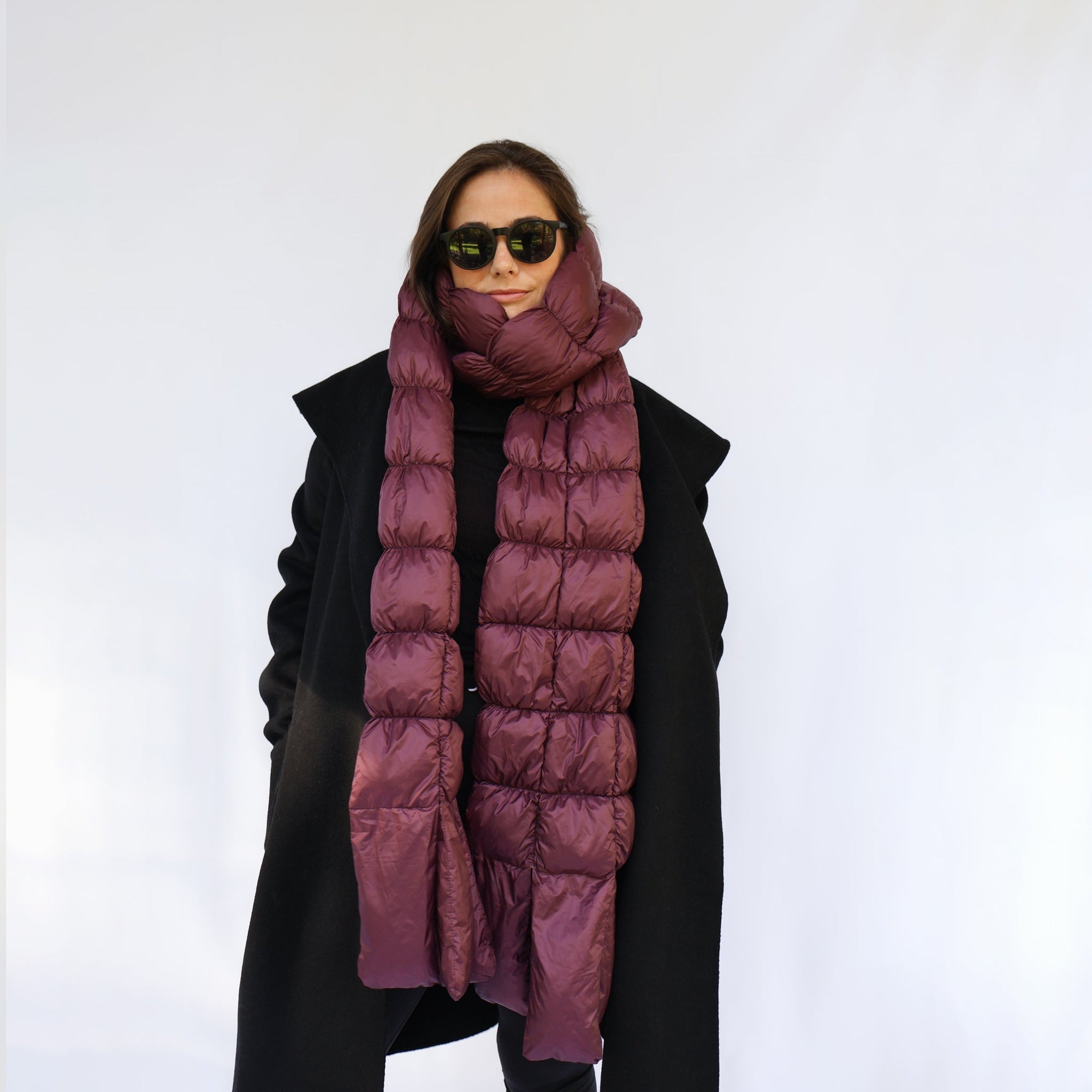 Model wearing a quilted puffer scarf in deep plum, draped over a black coat, front view