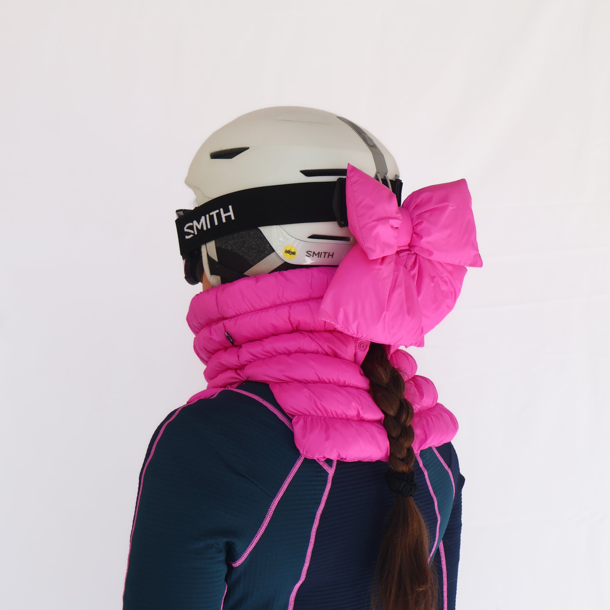Bright pink puffer ski helmet bow and neck gaiter worn with white ski helmet, side view