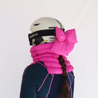 Bright pink puffer ski helmet bow and neck gaiter worn with white ski helmet, side view