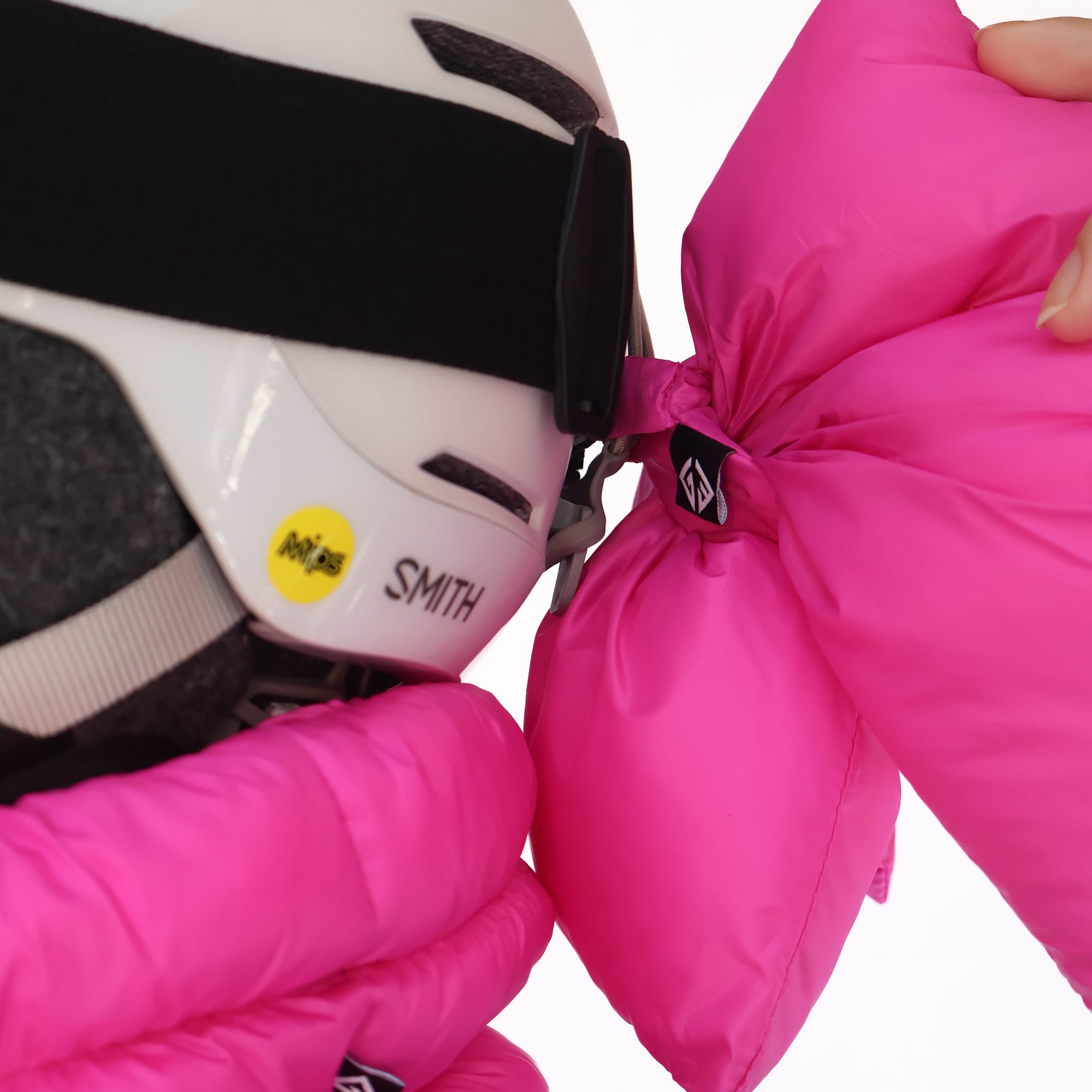 Bright pink ski helmet bow accessory being attached to a white ski helmet with goggles