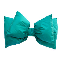 Large teal bow-shaped ski helmet accessory, puffy fabric, front view on white background