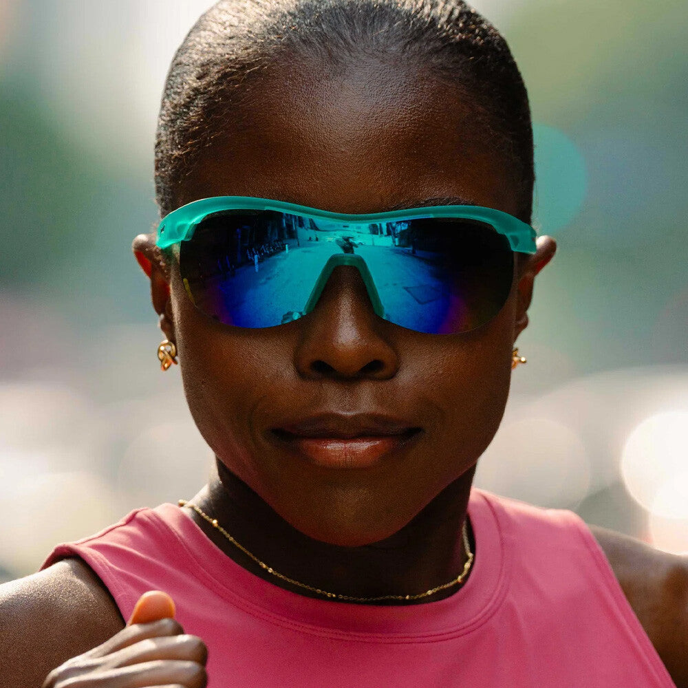 Turquoise wraparound sunglasses with blue mirrored lenses worn by person in pink athletic top
