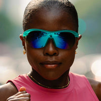 Turquoise wraparound sunglasses with blue mirrored lenses worn by person in pink athletic top
