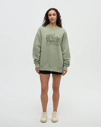 Light green crew neck sweatshirt with plant illustration graphic, worn by woman in studio setting