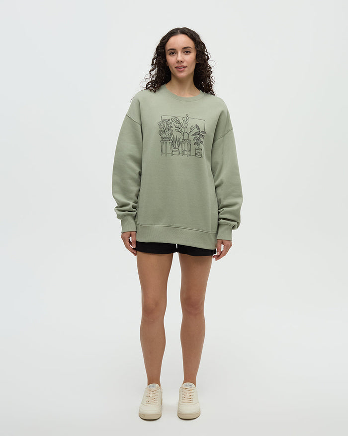 Light green crew neck sweatshirt with plant illustration graphic, worn by woman in studio setting