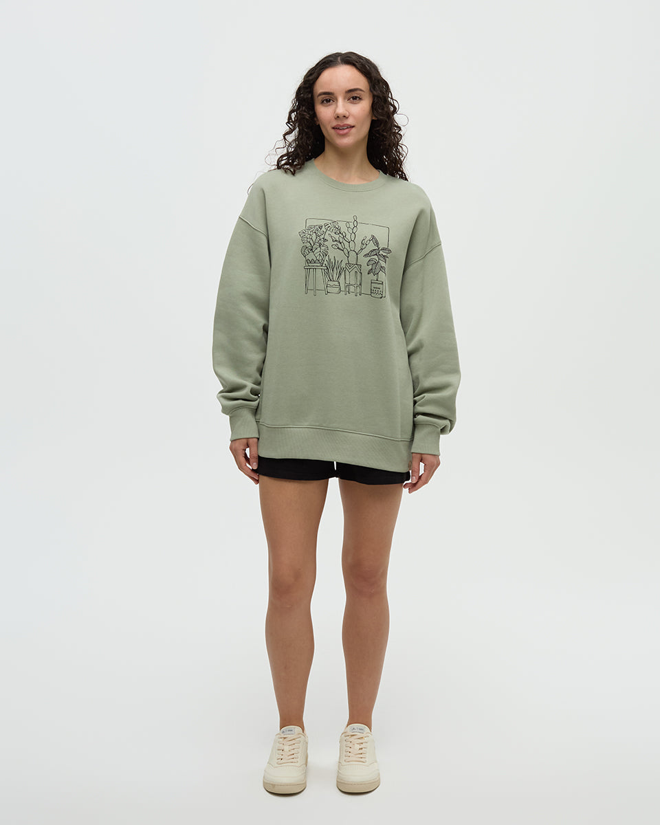 Light green crew neck sweatshirt with plant illustration graphic, worn by woman in studio setting