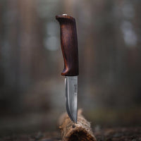 Fixed blade knife with curved dark wood handle standing upright on log surface