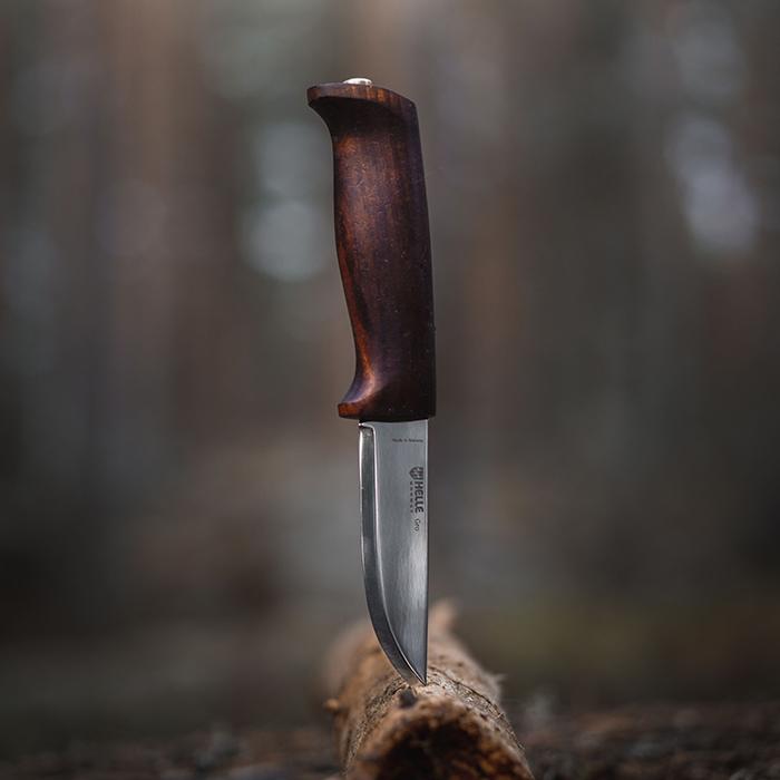 Fixed blade knife with curved dark wood handle standing upright on log surface
