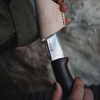 Fixed blade knife with carved wooden handle and black grip section being held outdoors