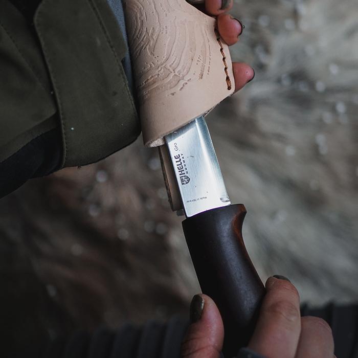 Fixed blade knife with carved wooden handle and black grip section being held outdoors
