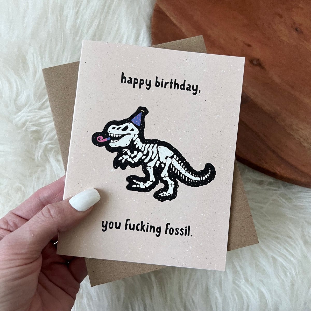 Humorous birthday greeting card with dinosaur skeleton illustration and profanity text message