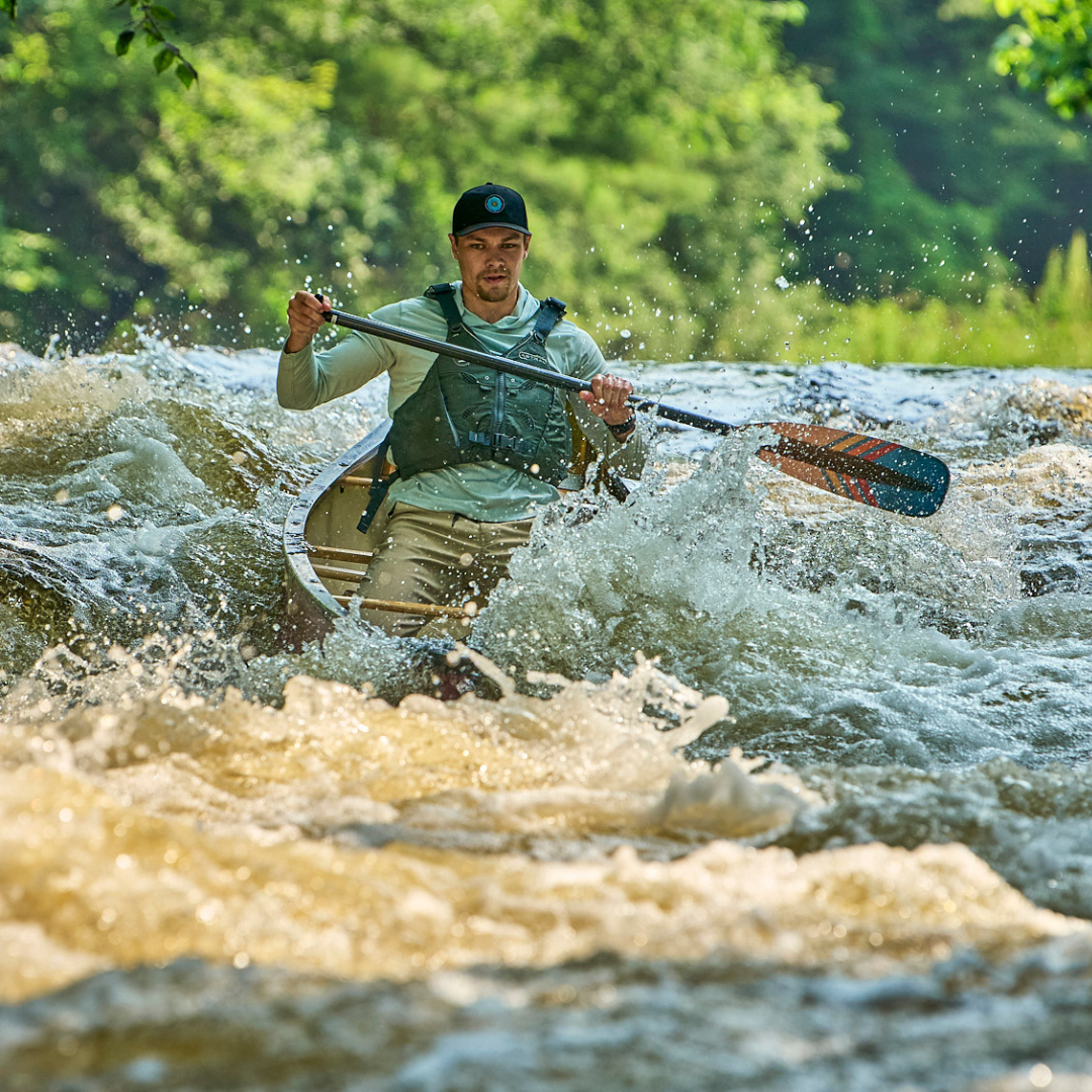 Canoe paddle with dark green blade and orange accent being used in whitewater rapids