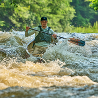 Canoe paddle with dark green blade and orange accent being used in whitewater rapids