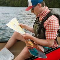 Canoe paddle with orange and teal striped blade held by person in canoe on water