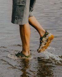 Water shoes with olive green and tan colorway splashing through shallow water on wooden dock