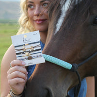 Set of four hair tie bracelets with equestrian charms displayed on packaging card, held by model near horse