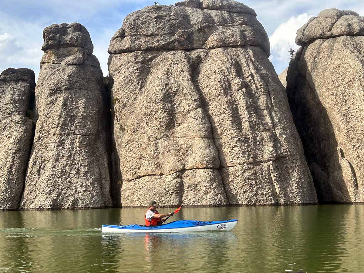 Blue sea kayak with paddler navigating calm water alongside tall rock formations