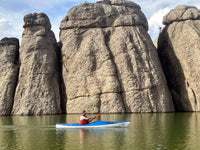 Blue sea kayak with paddler navigating calm water alongside tall rock formations