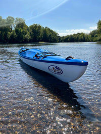 Blue and white kayak floating in shallow water with trees in background