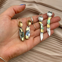 Hand holding two pairs of miniature pocket knife dangle earrings with abalone shell inlay, one gold and one silver
