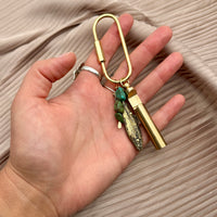 Gold brass carabiner keychain charm with turquoise stones, fish pendant, and cylindrical vial held in hand