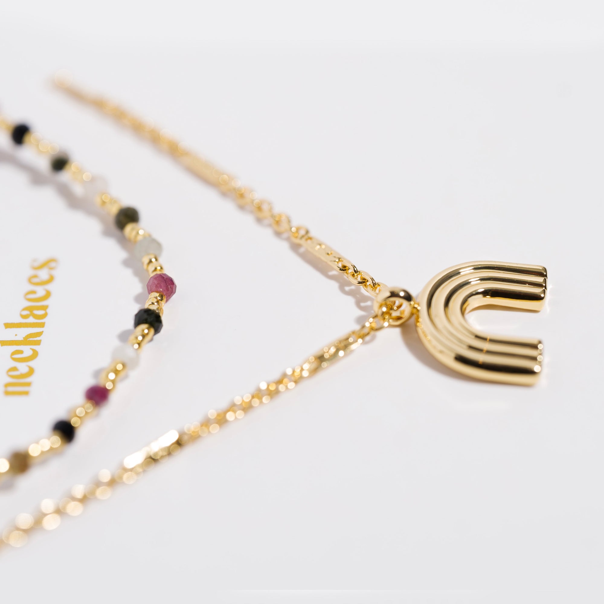 Gold necklace set with multicolor gemstone beads and a gold rainbow arc pendant, macro detail shot