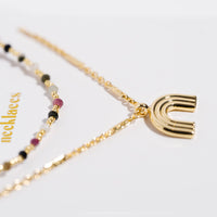 Gold necklace set with multicolor gemstone beads and a gold rainbow arc pendant, macro detail shot