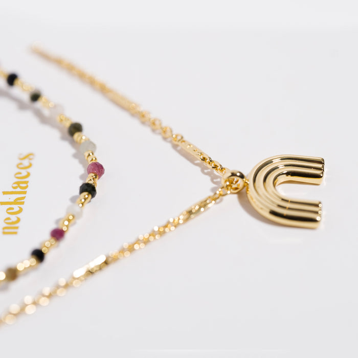 Gold necklace set with multicolor gemstone beads and a gold rainbow arc pendant, macro detail shot