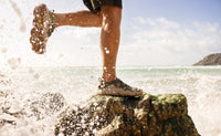 Water shoe on rocky surface with ocean waves splashing around foot
