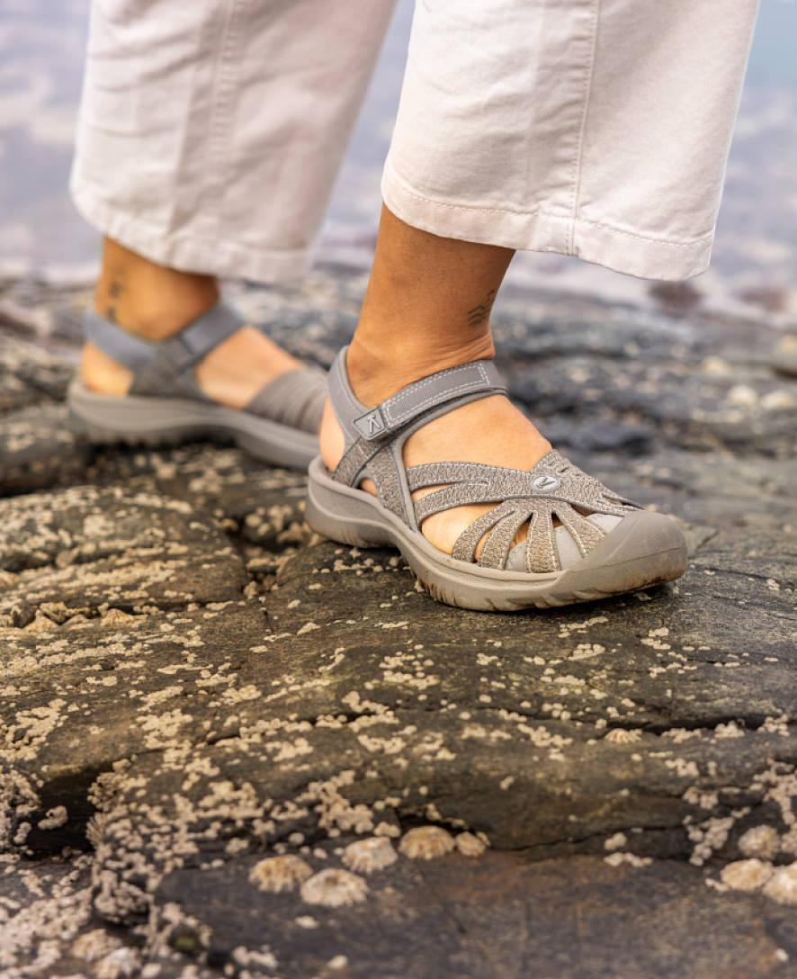 Gray closed-toe sport sandals with adjustable straps worn on rocky outdoor terrain