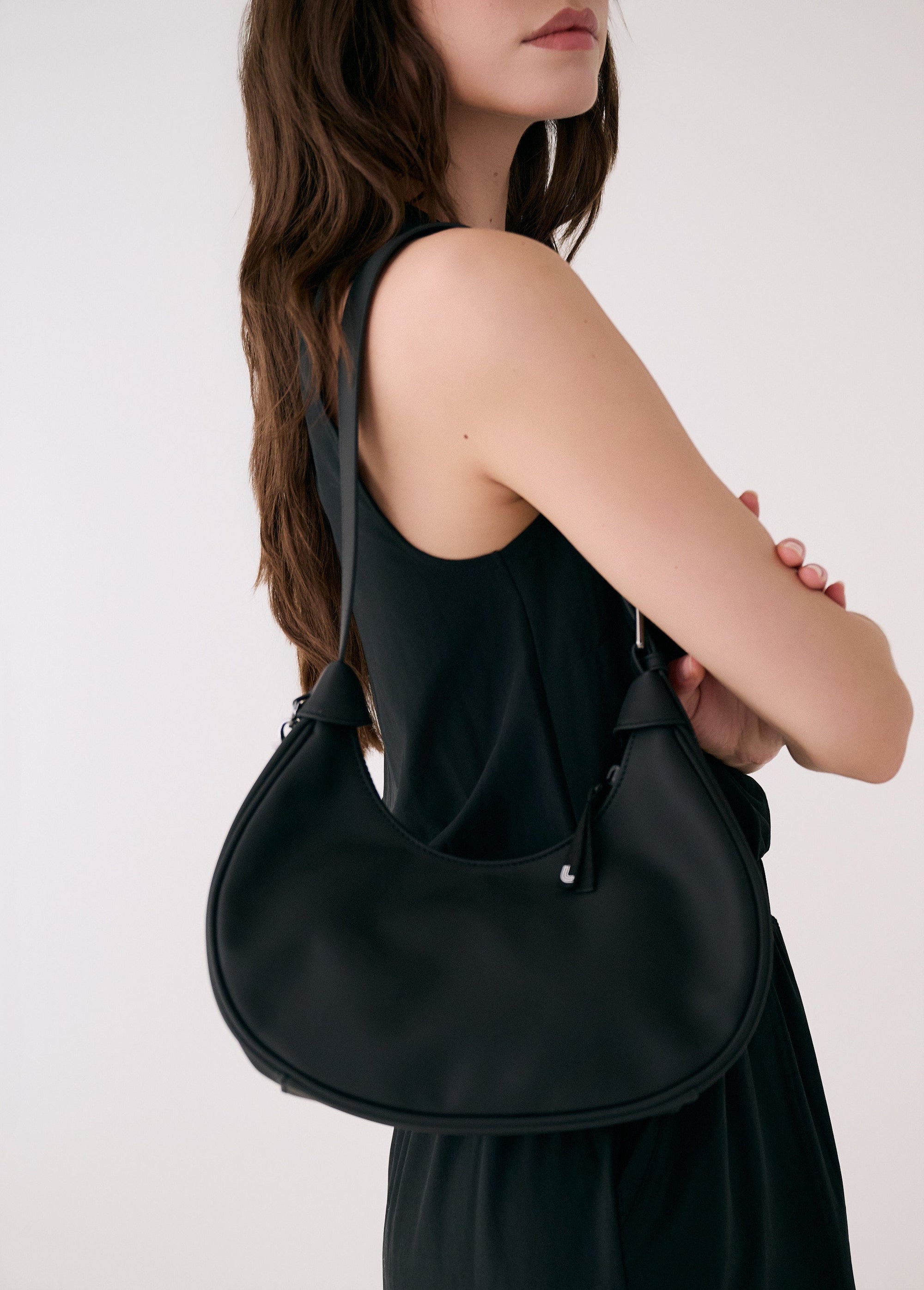 Black hobo bag worn on shoulder by woman in matching dress against white background